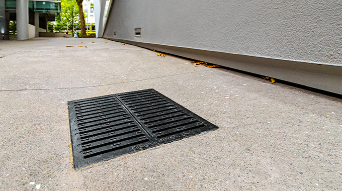 Allproof square plastic drainage pit with cast iron grate installed in concrete